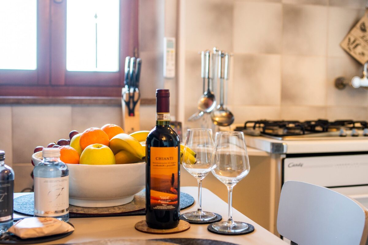 Cucina di Ipazia con bottiglia di vino, calici e cesto di frutta fresca