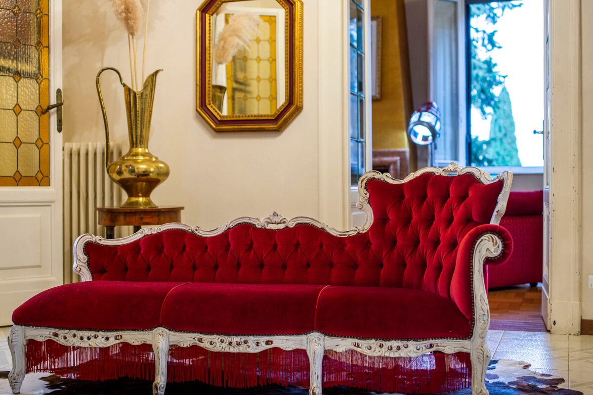 Divano in velluto rosso capitonné e specchio dorato in un salotto della villa